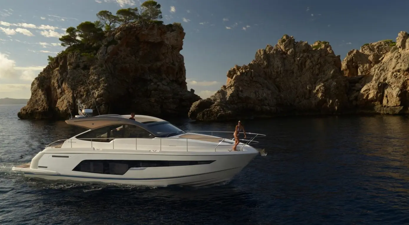 A luxury motor yacht navigates calm waters near rugged cliffs, with a woman standing on the bow, enjoying the scenery.